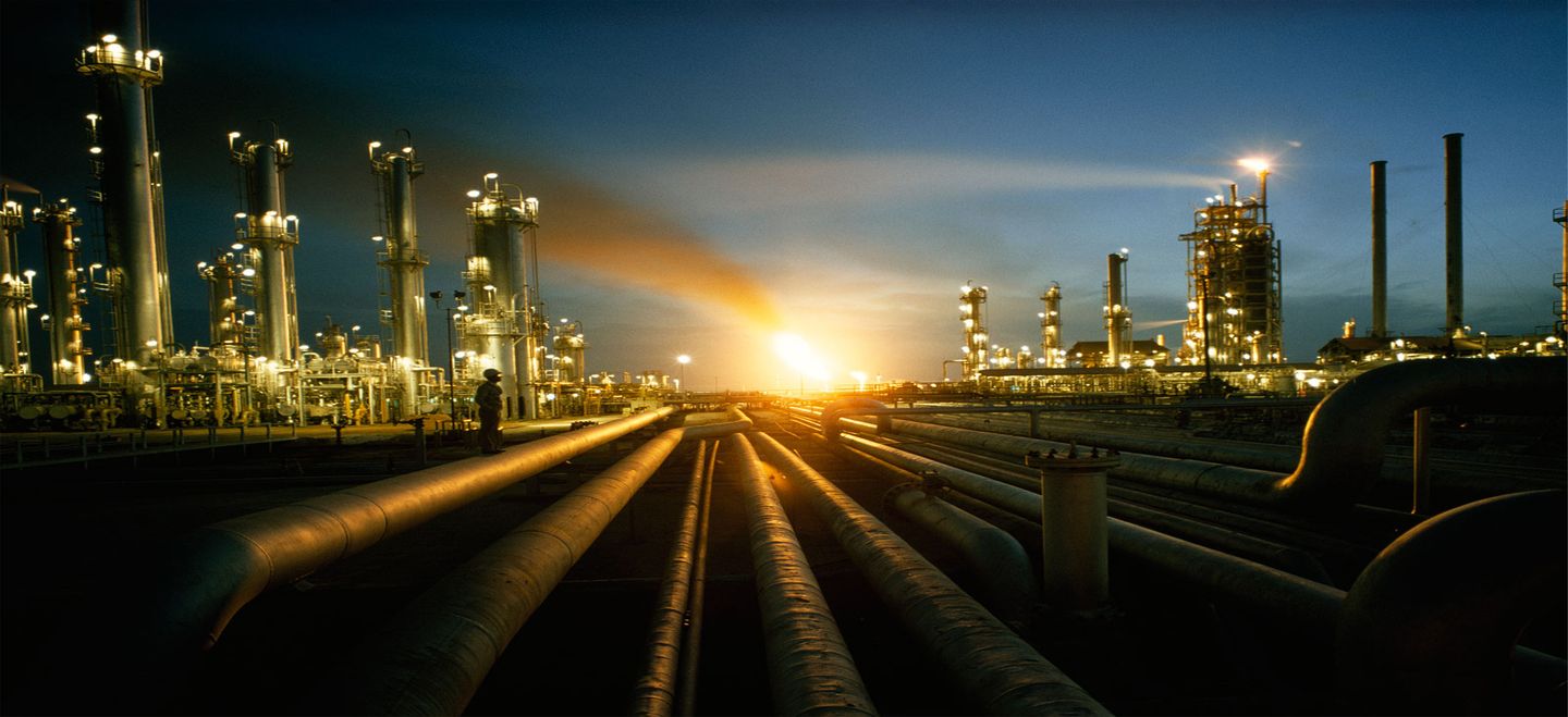 Process plant at dusk with buried and above-ground pipelines converging toward a flare