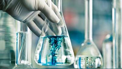A gloved hand dosing a blue reagent into a laboratory flask