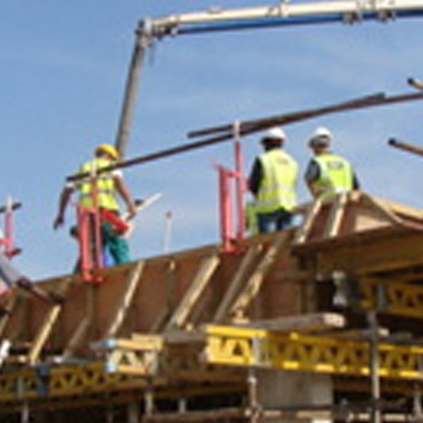 Workers placing formwork on a raised concrete deck, with a crane above