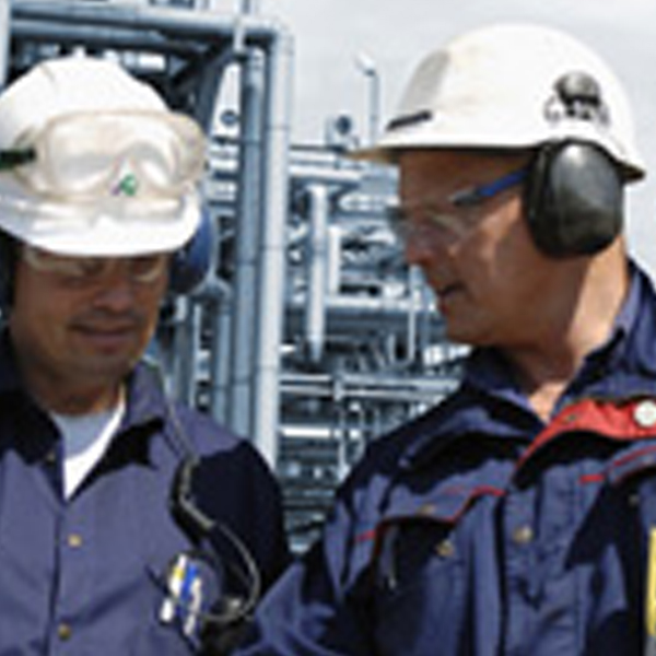 Two workers in hard hats and ear defenders at a process plant