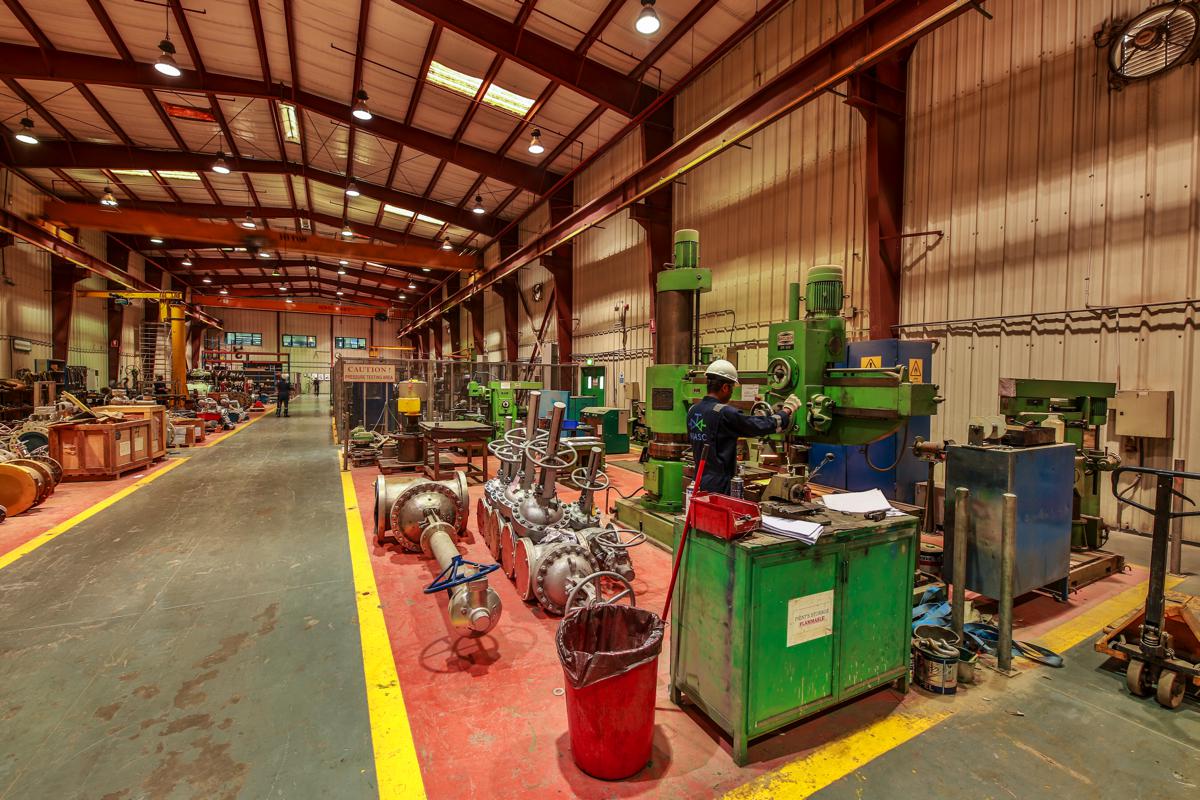 A technician at a radial arm drill in the machining area, valves lined up alongside