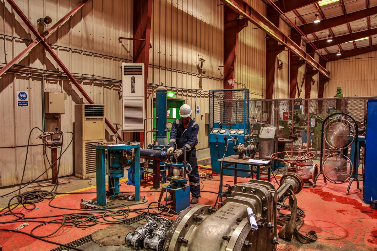 A technician at a test rig fitted with pressure gauges, a large flanged valve in the foreground