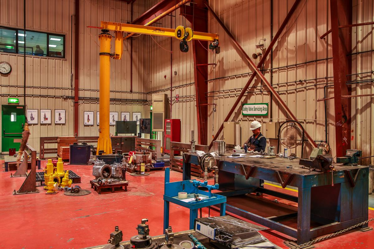 A technician at the workbench in the safety valve servicing area, beneath a yellow jib crane