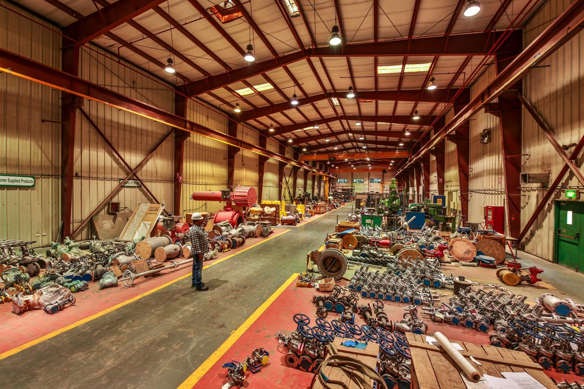 A technician crossing the workshop walkway, valves laid out on the red floor either side