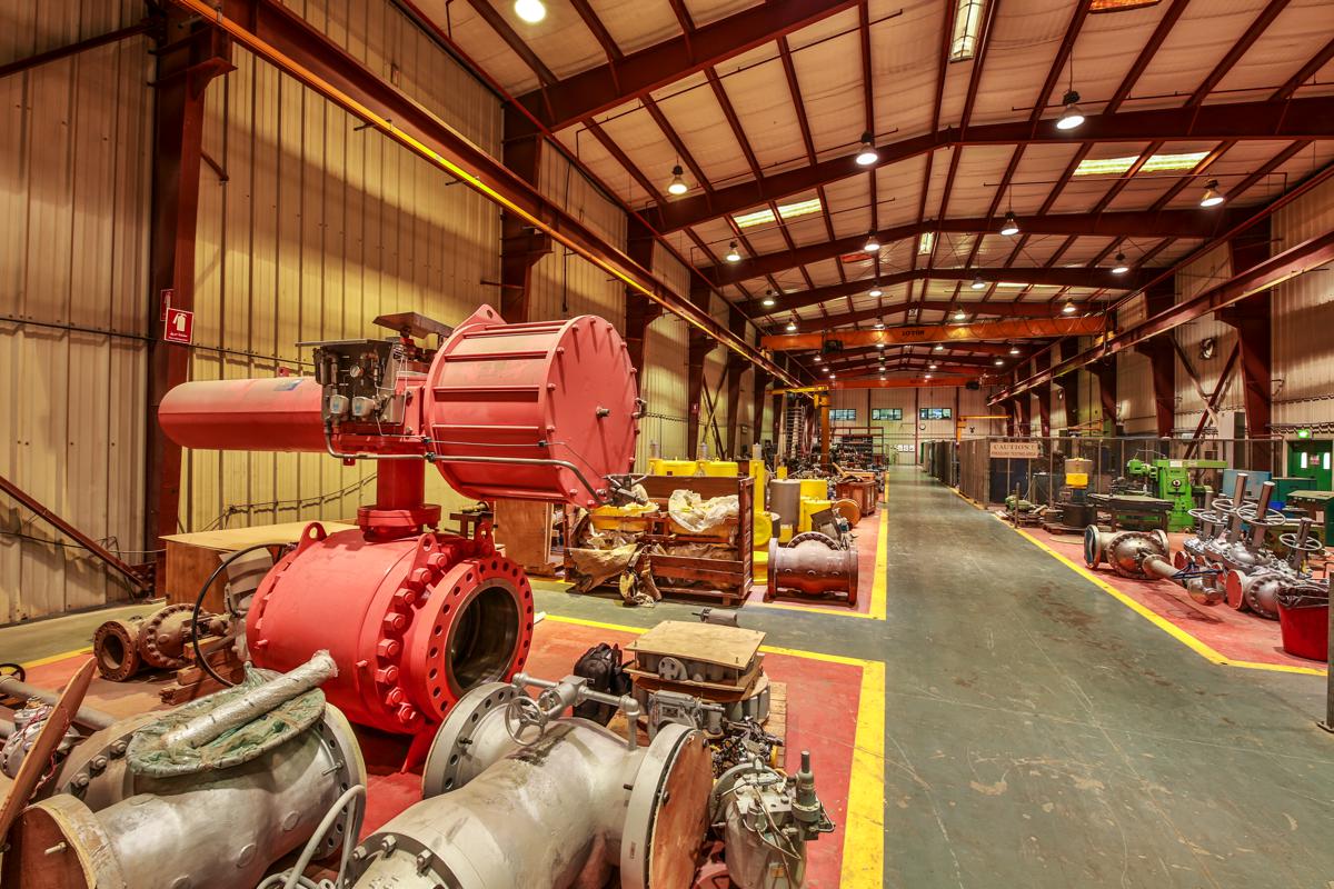 A large red actuator mounted on a ball valve in the foreground of the workshop bay
